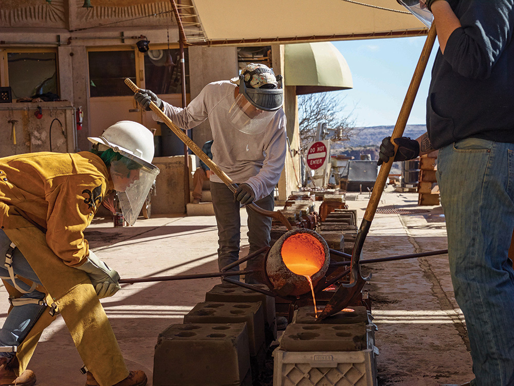 Workers pour molten bronze, heated to 1,315ºC, into sand moulds. The green umbrella in the background collects waste heat from the furnace to warm the surrounding residential apartments